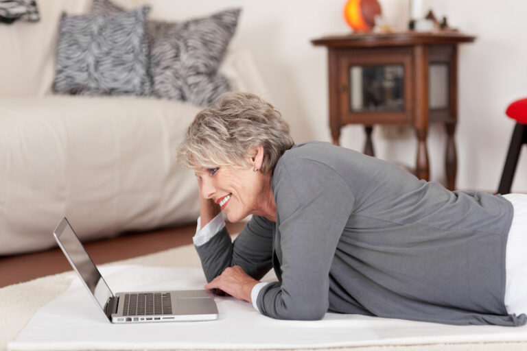 Older woman lying on the floor using a laptop