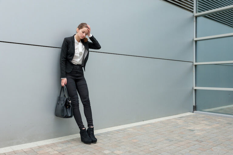 Young woman leaning against a wall, clearly upset