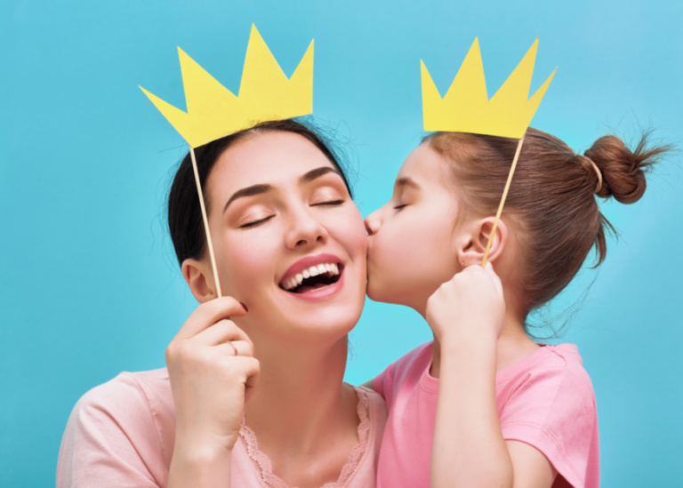 Young daughter kissing mother on the cheek, both wearing paper crowns