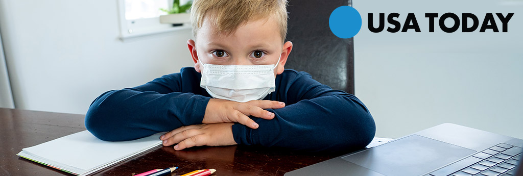 Kid wearing a face mask and sitting at a computer with a laptop and USA TODAY in top right corner of the image